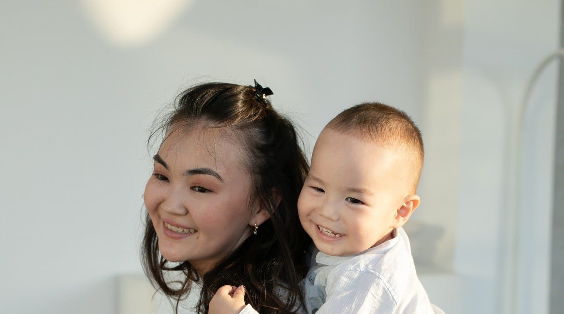 A mother laughing with her son as he rides on her back